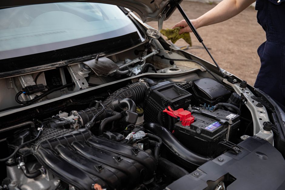 Smiling auto repair technician standing proudly next to a vehicle